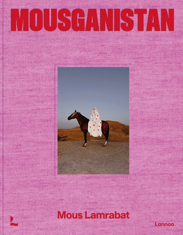 Pink linen book cover of Mous Lamrabat’s Mousganistan, with a figure in white robe sitting on horse surrounded by desert. Published by Lannoo Publishers.