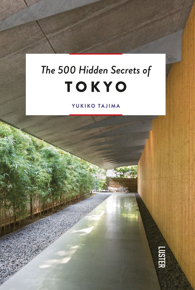 Walkway under building roof ledge, line of bamboo trees to left, The 500 Hidden Secrets of Tokyo in black font on white banner