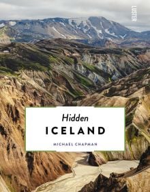 Aerial view of gold, blue and green mountainous landscape, Hidden Iceland in black font on white banner below