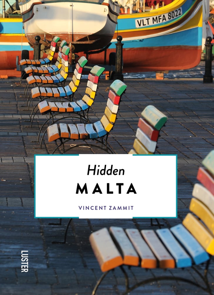 Row of multicoloured slated wood chairs, near harbour edge, with boat, Hidden MALTA in black font on bottom white banner.