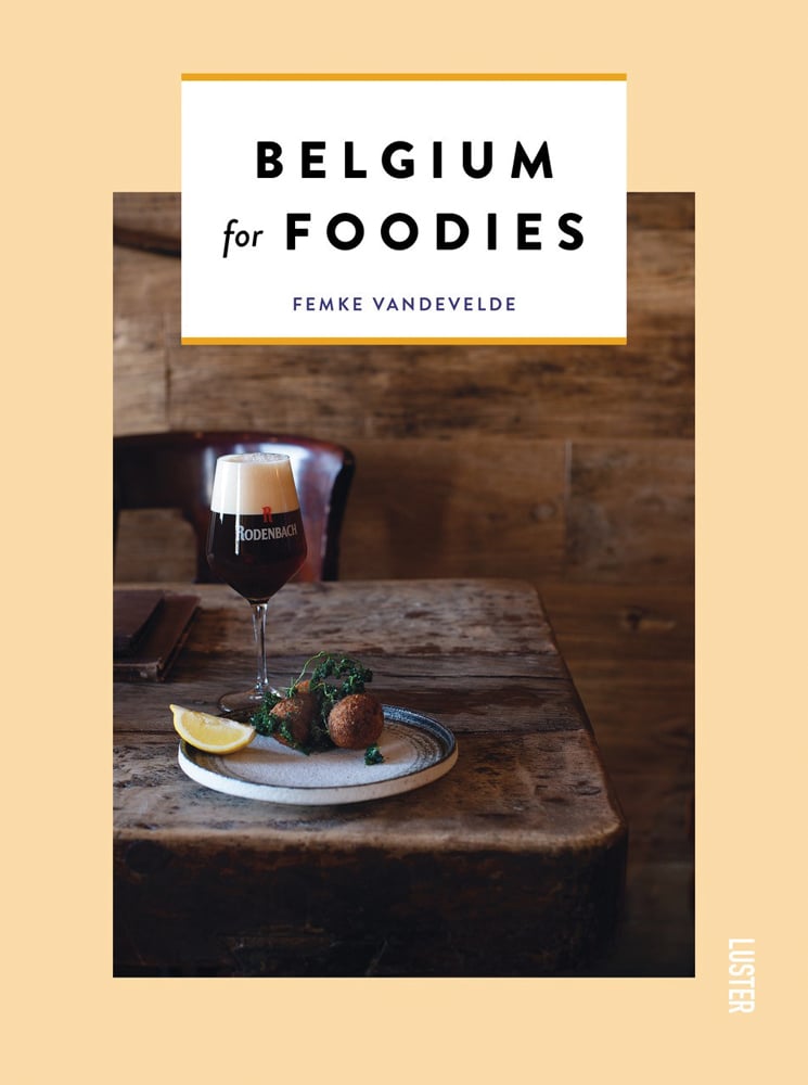 Beige cover with plate of fried food with kale and lemon slice with glass of beer on walnut table with Belgium for Foodies in black font on white banner