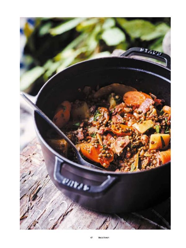 Woman sitting in doorway of campervan with black dog, in forest area, on cover of 'Camper Food & Stories', by Luster Publishing.