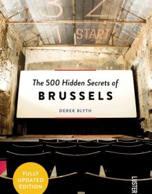 Colour photo of a view from a cinema seat in a derelict theatre, looking at a white screen with The 500 Hidden Secrets of Brussels in black font