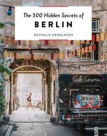 Book cover of The 500 Hidden Secrets of Berlin, with Café Cinema bench with bunting and street art. Published by Luster Publishing.