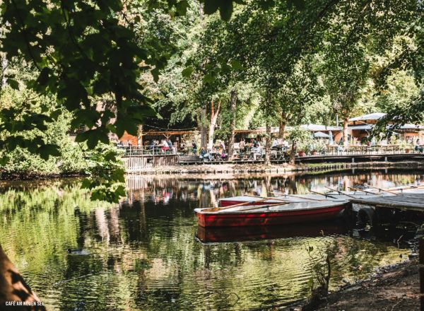 Book cover of The 500 Hidden Secrets of Berlin, with Café Cinema bench with bunting and street art. Published by Luster Publishing.