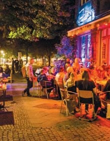 Book cover of The 500 Hidden Secrets of Berlin, with Café Cinema bench with bunting and street art. Published by Luster Publishing.