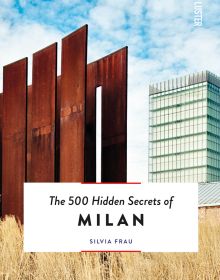 Tall rusted metal paneled structure surrounded by pale dry grass, tall building behind, on cover of 'The 500 Hidden Secrets of Milan', by Luster Publishing.