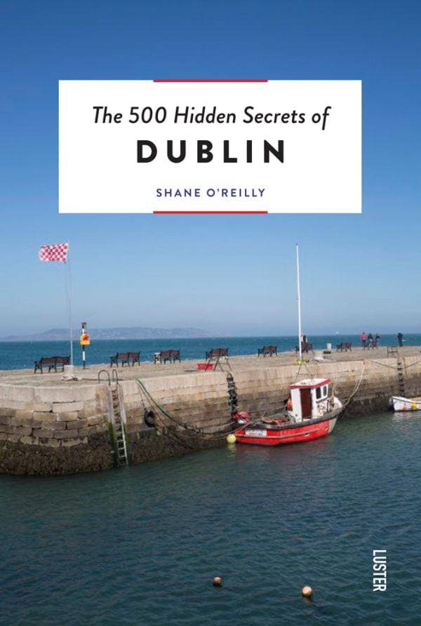 Book cover of The 500 Hidden Secrets of Dublin, with a fishing boat at Bulloch Harbour, Dalkey, under blue sky. Published by Luster Publishing.