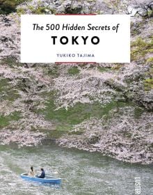 Book cover of The 500 Hidden Secrets of Tokyo, with a couple in boat on Imperial Palace moat, rowing beneath pink blossom trees. Published by Luster Publishing.