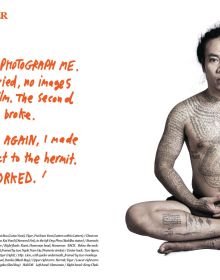 Asian male, hands on hips, serious face, with torso covered in finely detailed black tattoos, SACRED SKIN Thailand's Spirit Tattoos in orange font above.
