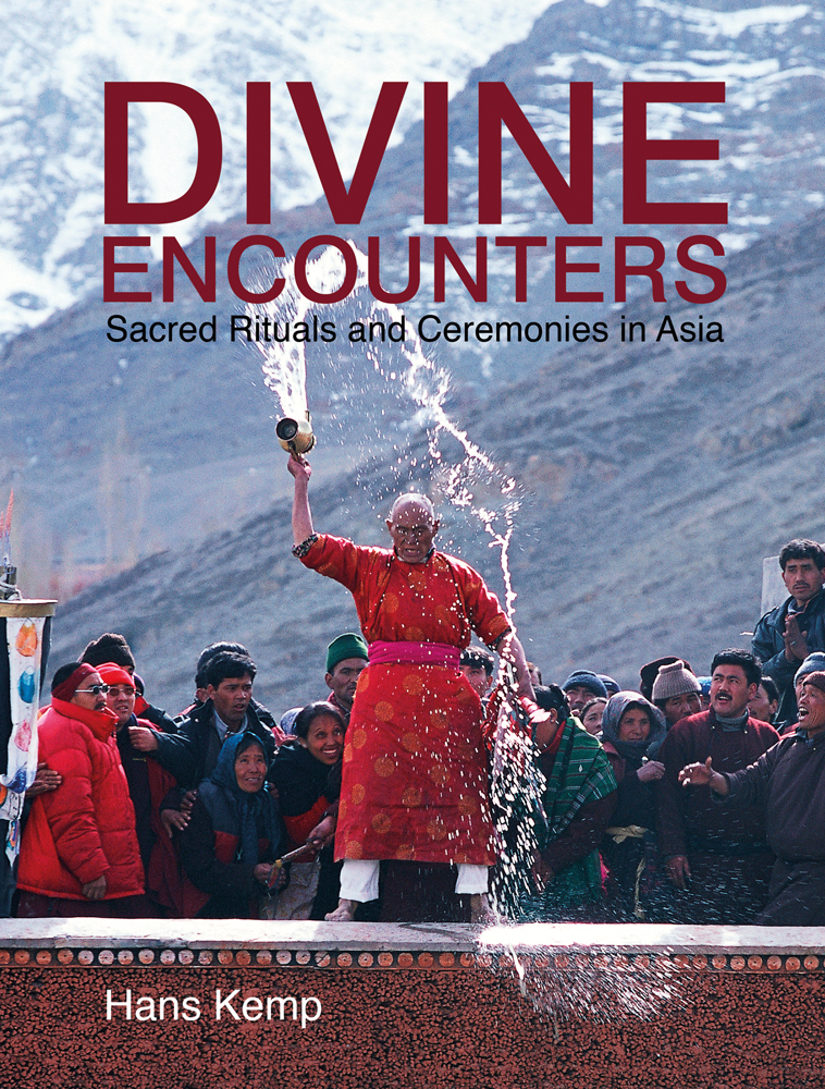 Asian ritual performed by male in orange dress, throwing water from brass jug, mountain scape behind, DIVINE ENCOUNTERS in dark red above.