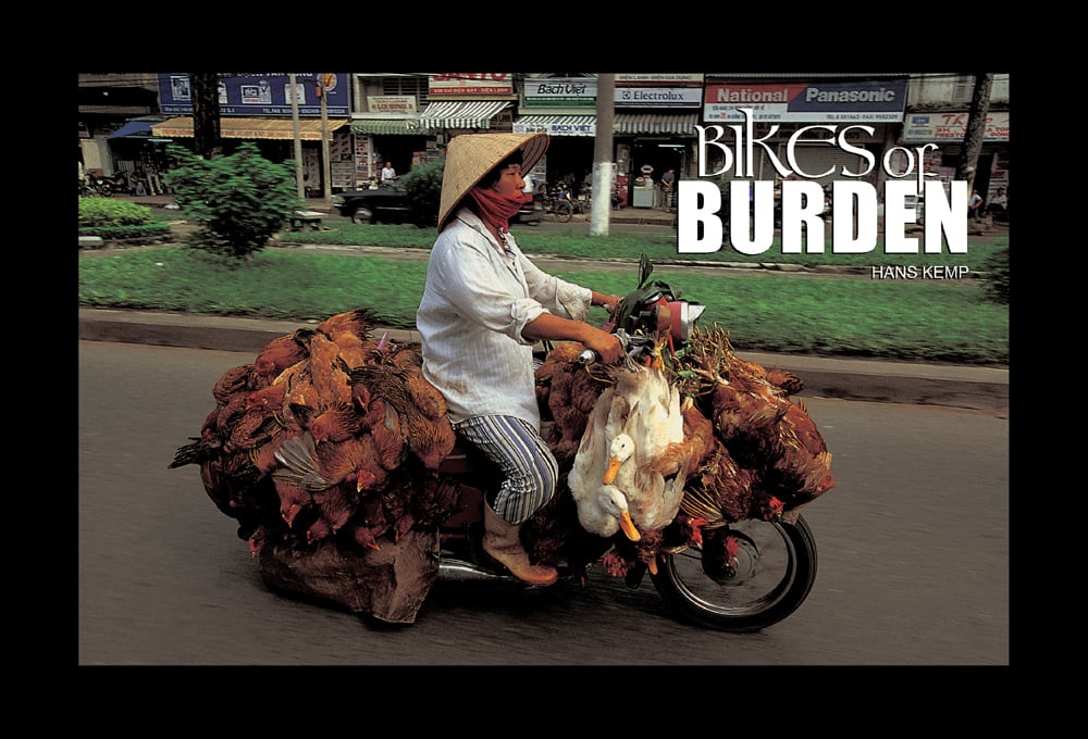 Vietnamese street vendor riding motorbike weighed down with dead chickens and geese, black border, Bikes of BURDEN in white font to upper right.